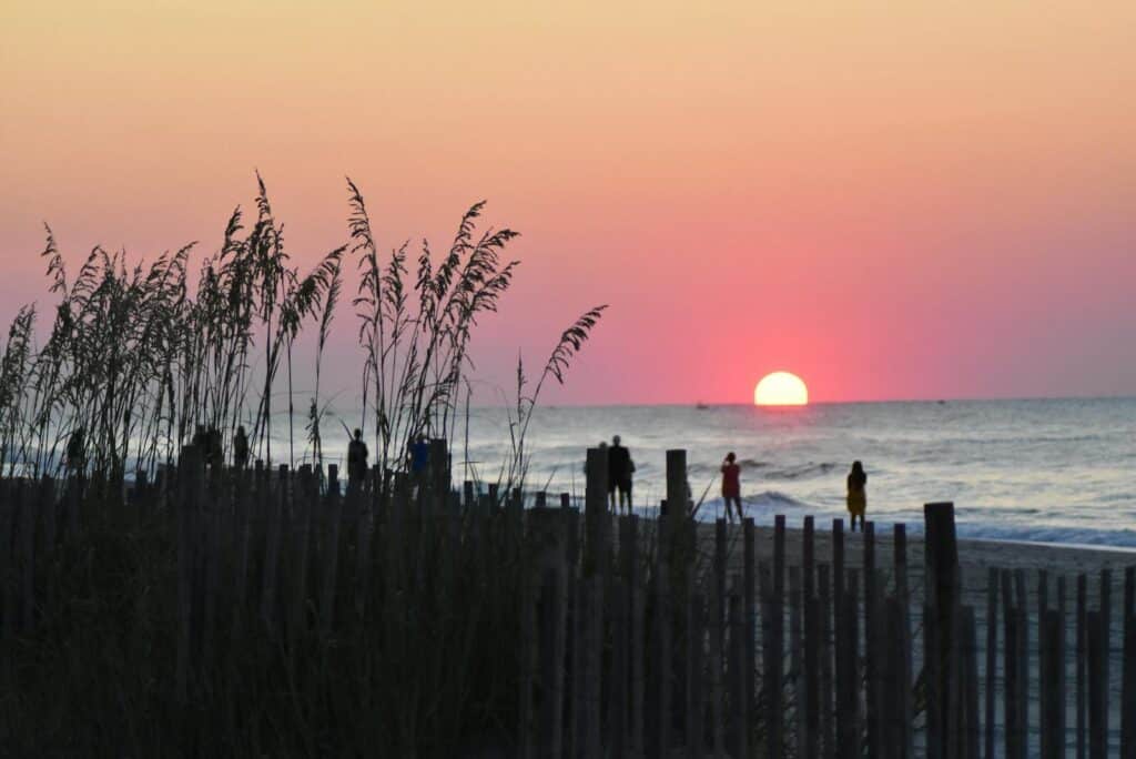 A peaceful sunrise at Myrtle Beach with silhouettes of people on the shoreline creating a tranquil scene.