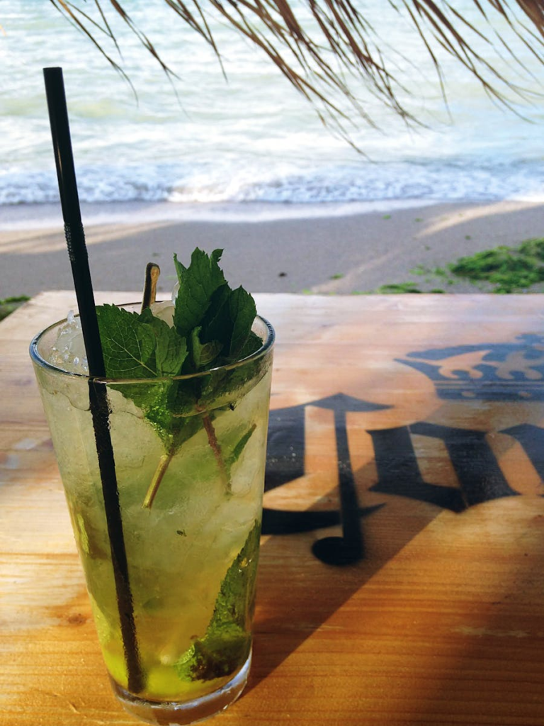 A refreshing mojito cocktail on a beachside table with a scenic ocean view in the background.