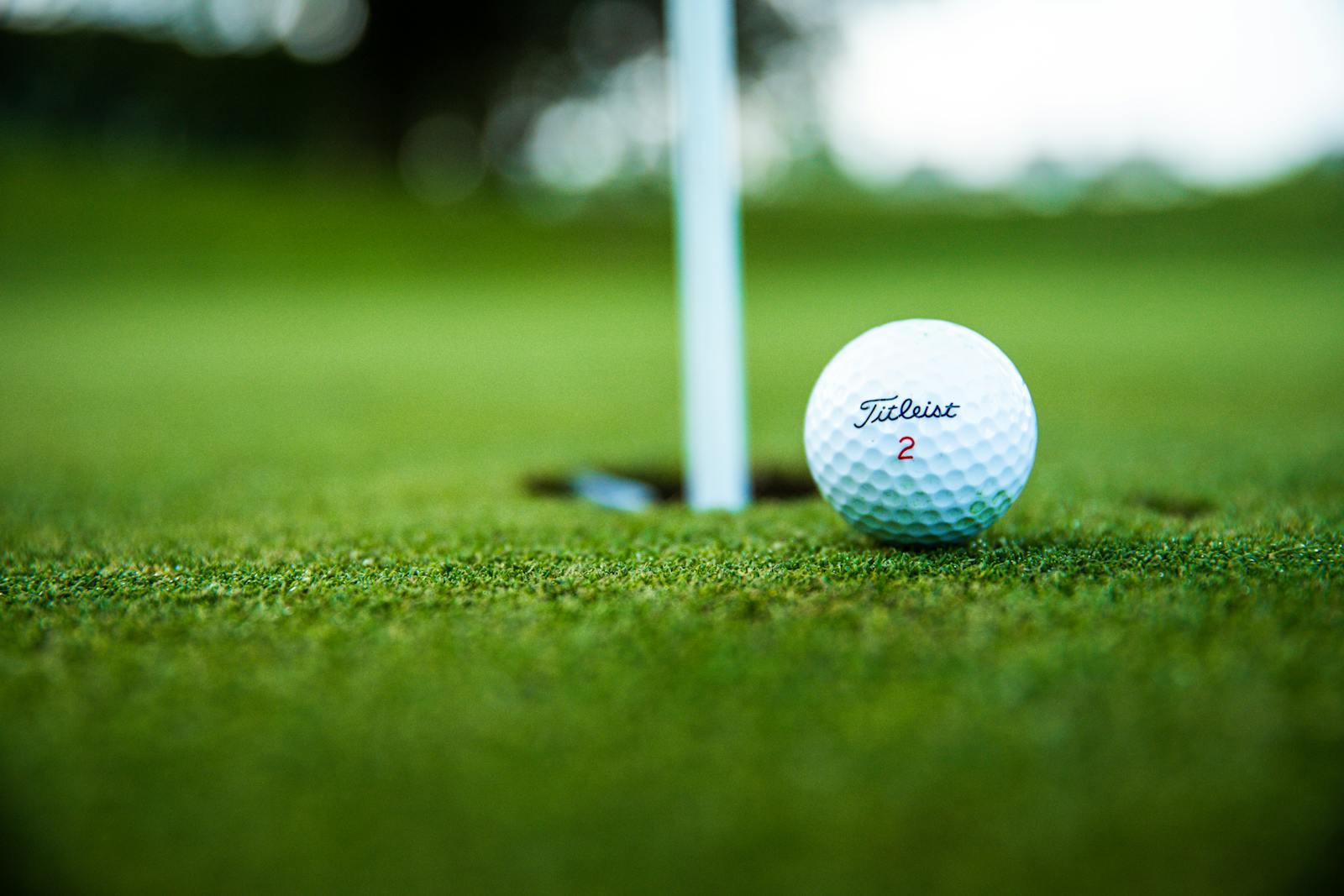 A close-up shot of a Titleist golf ball close to the hole on a green golf course. popstroke myrtle beach