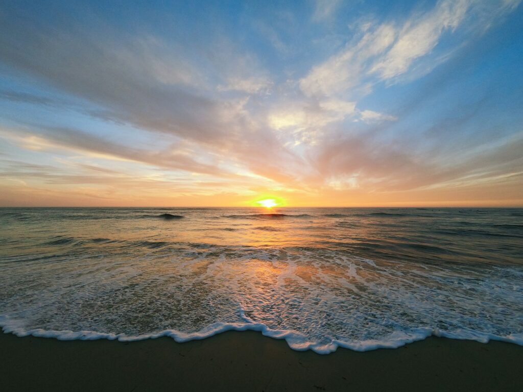 the sun is setting over the ocean on the beach