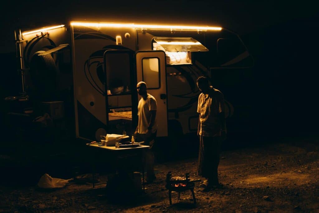 Two adults camping at Showkah, UAE with a lit caravan and outdoor cooking at night.