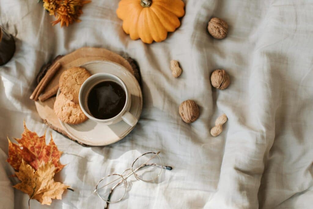 Warm autumn scene featuring coffee, cookies, walnuts, and pumpkin on a cozy cloth background.