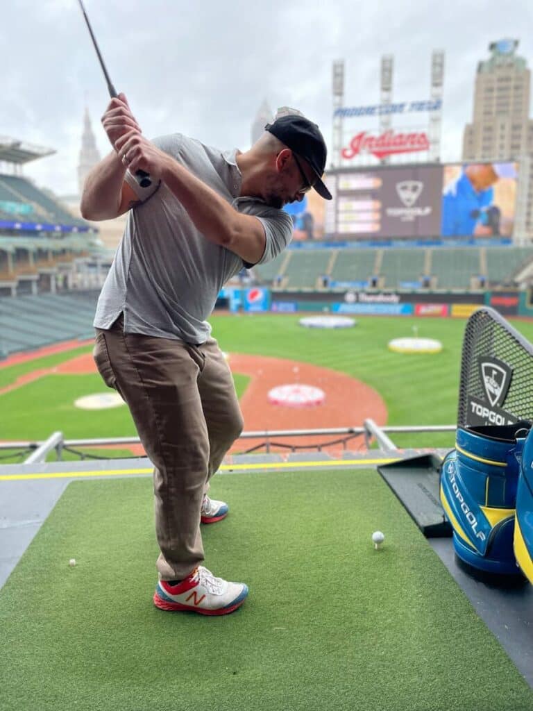 Man practicing golf swing at a baseball stadium golf range in Cleveland.