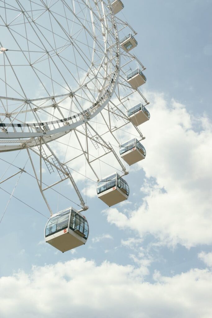 Close-up of a Ferris wheel under a clear, cloud-dotted sky captured in a vertical shot.
