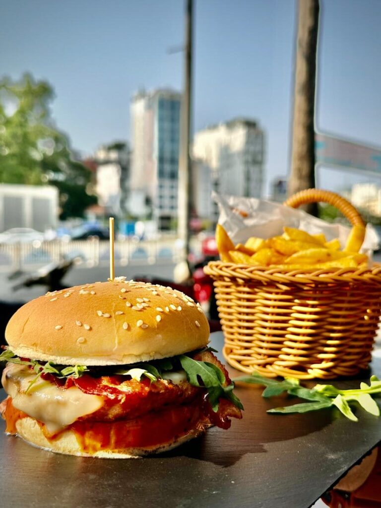Juicy burger with arugula and cheese, served with fries on a sunny day in Ho Chi Minh City.