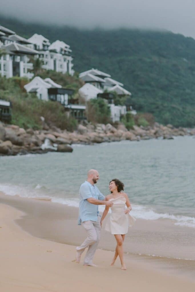 Couple walking on a sandy beach near ocean.
