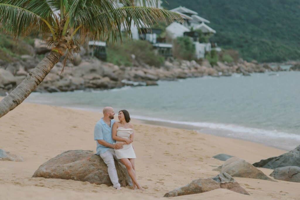 Couple embracing on a sandy beach near rocks.