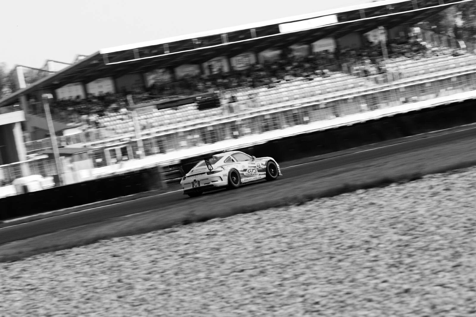 Exciting black and white capture of a sports car racing on a track, showcasing speed and action.