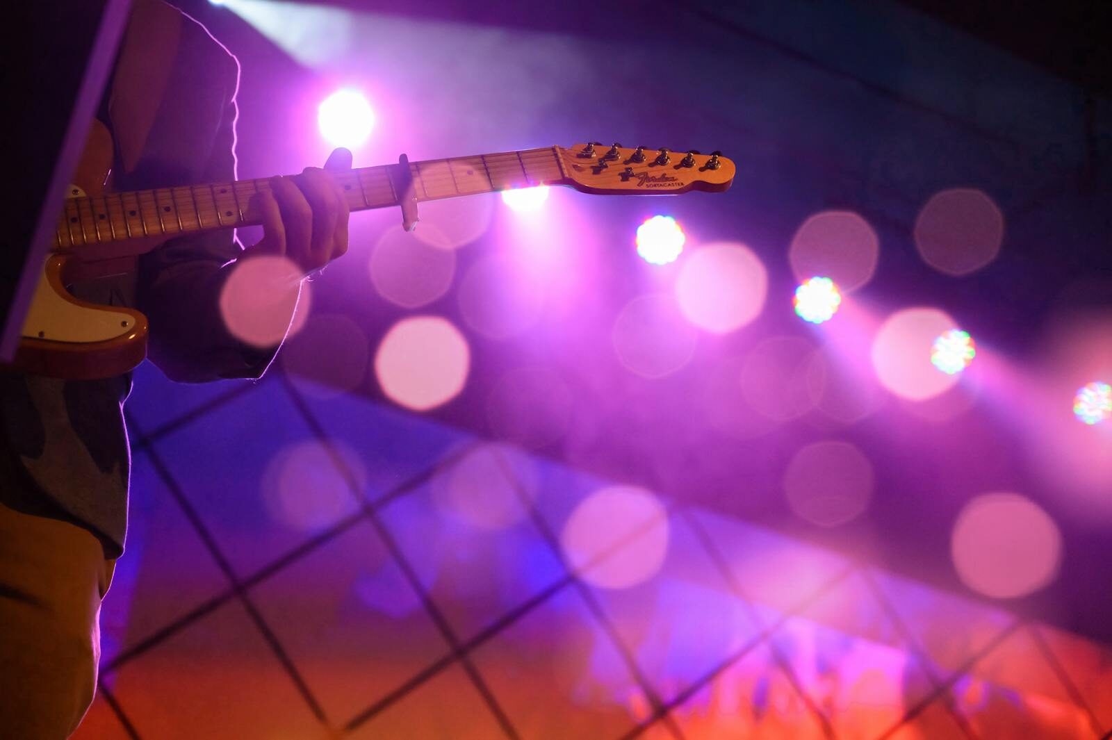 Close-up of a guitarist performing on stage with colorful lights and bokeh effects.