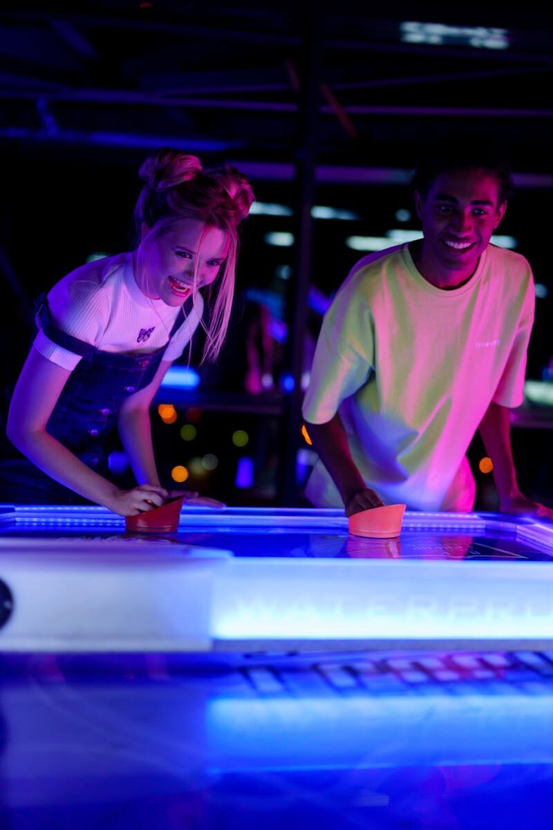 Two young friends having fun playing air hockey in a neon-lit amusement arcade.
