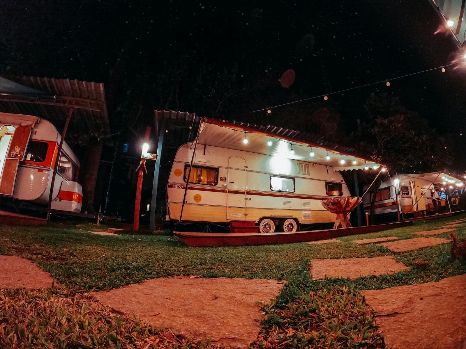 Cozy, illuminated caravans in a nighttime park setting, perfect for travel and adventure enthusiasts.