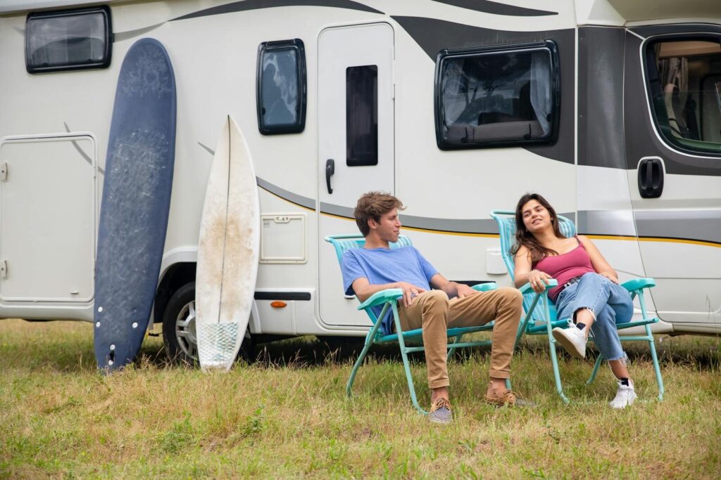 Couple relaxing by an RV with surfboards on a grass field, enjoying leisure time in Portugal.