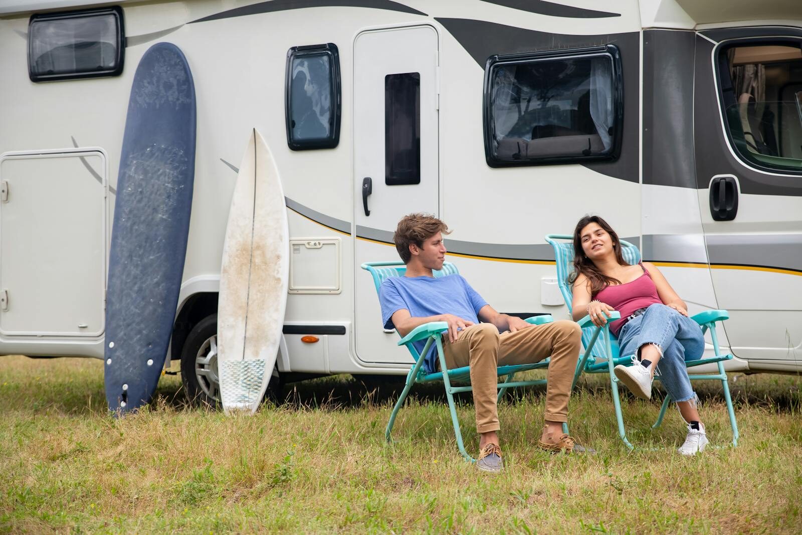 Couple relaxing by an RV with surfboards on a grass field, enjoying leisure time in Portugal.