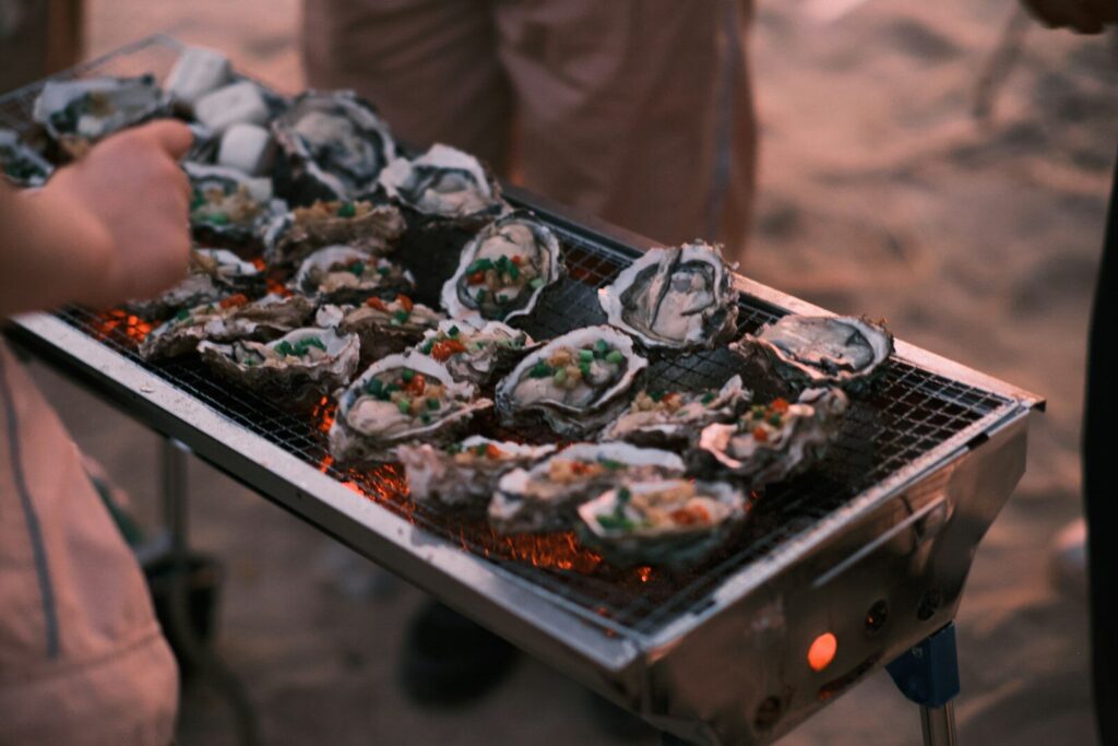 a person holding a tray of oysters on a grill