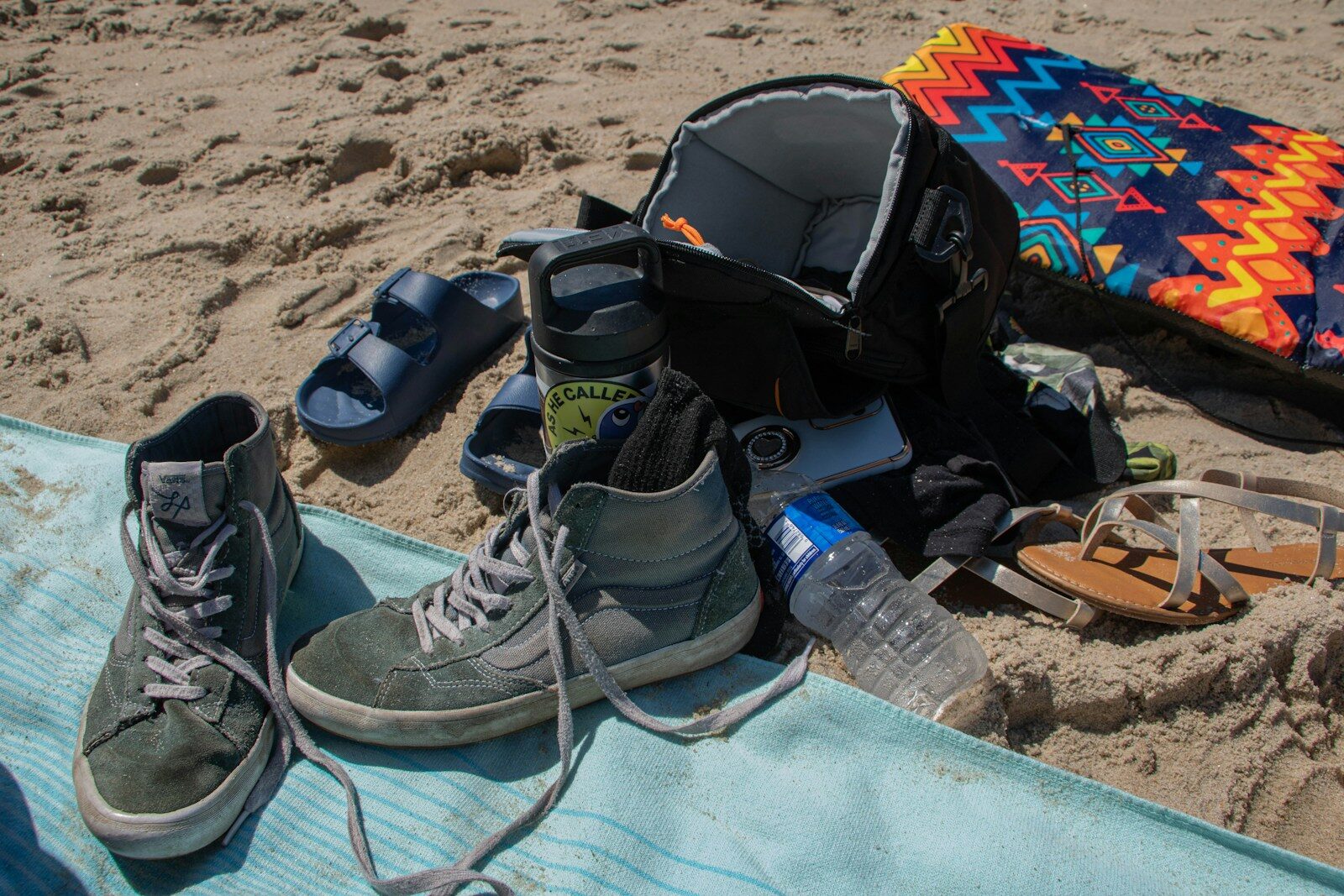 Beach gear laid out on sand with backpack and shoes.