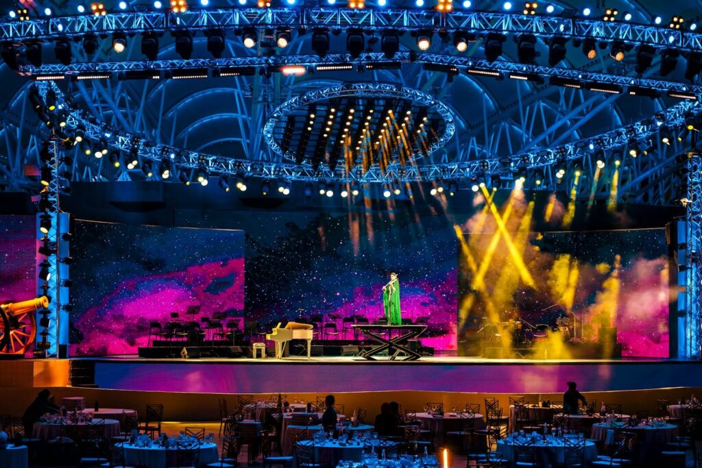 A performer plays piano on a brightly lit stage.